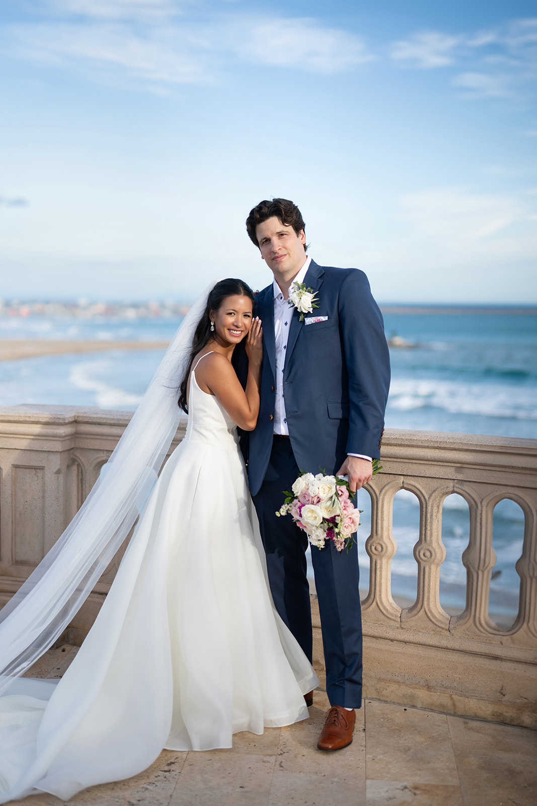 Bride and groom on a stone balustrade above the sea near Sitges in the late afternoon