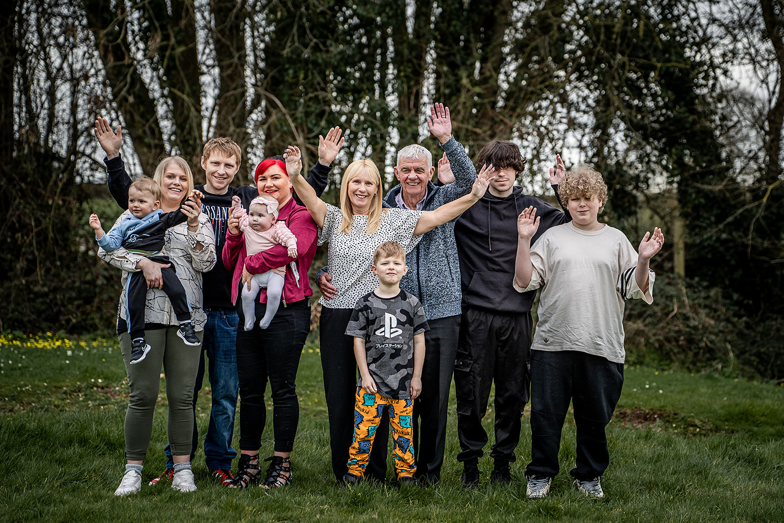 A large family group smiling and waving in a woodland clearing