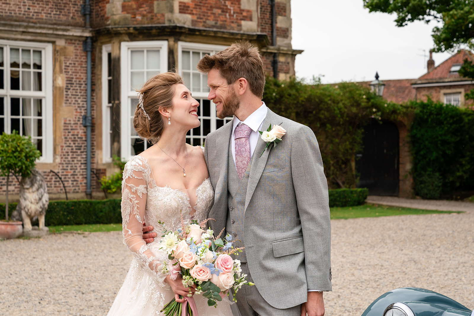 Harriet and Jared smiling outside Goldsborough Hall beside their vintage car