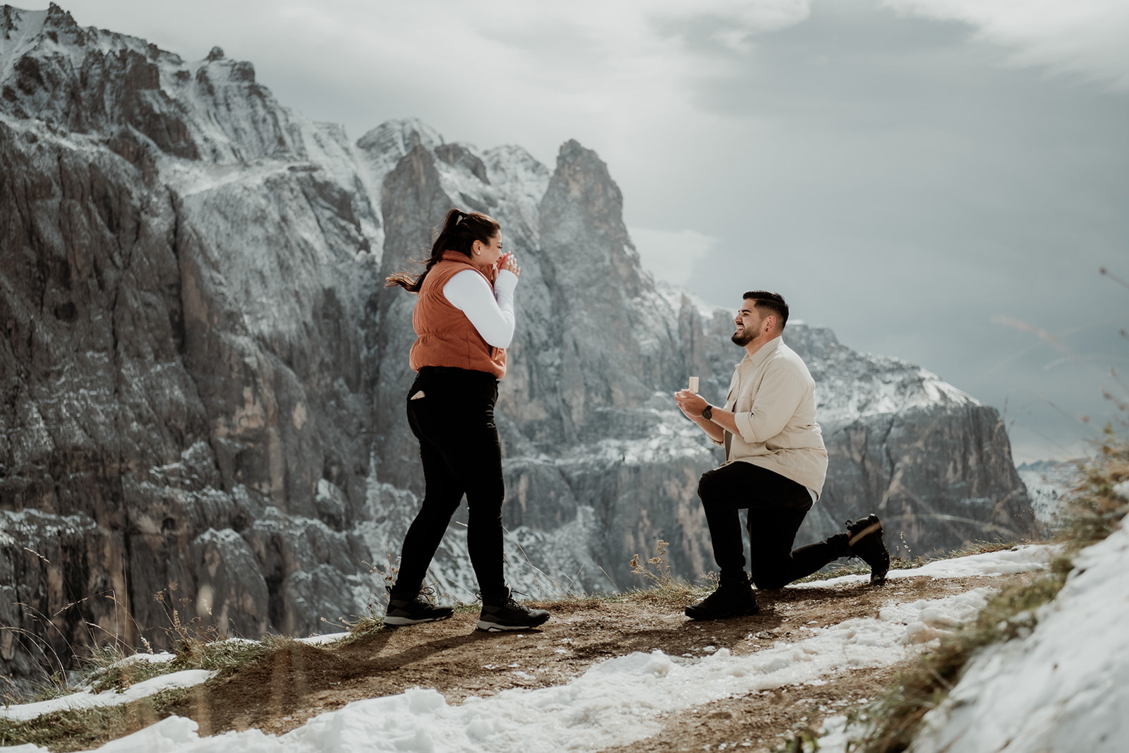 Candid engagement photo with dramatic Dolomites peaks in the background in the snow - a proposal in the Dolomites