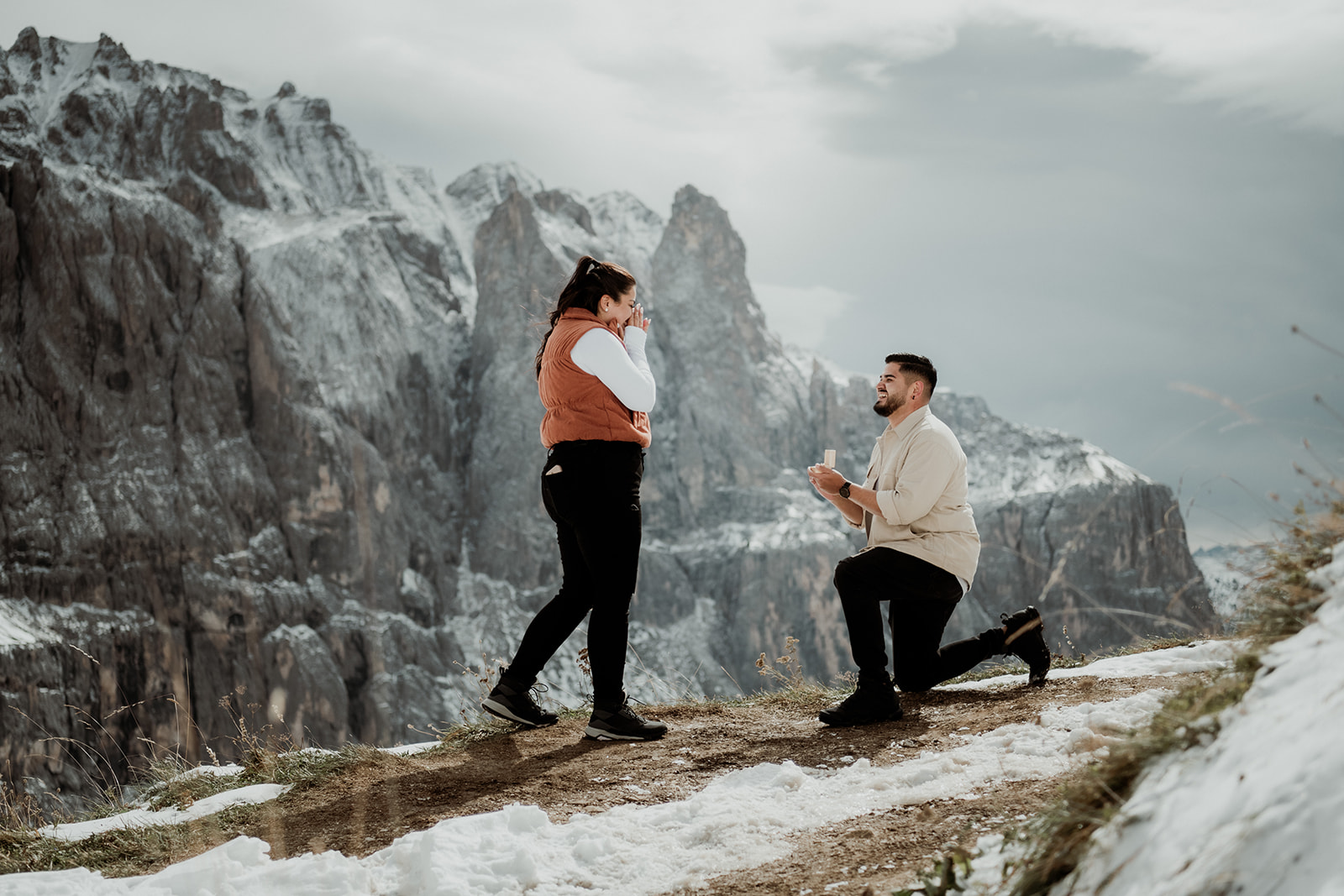 Heiratsantrag in den Bergen im Winter, Frau wird von ihrem Mann überrascht in der Winterlanschaft und Dolomiten im Hintergrund