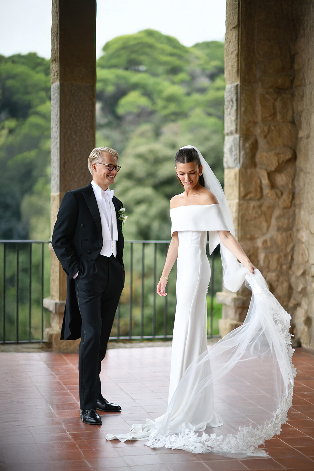 Bride and groom under the stone arches of La Baronia with green hills behind