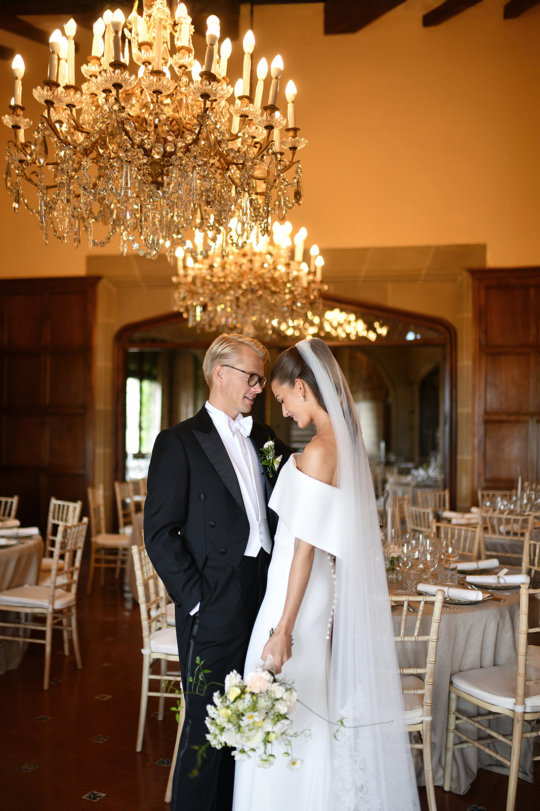 Bride and groom under the chandeliers of the dining hall at La Baronia