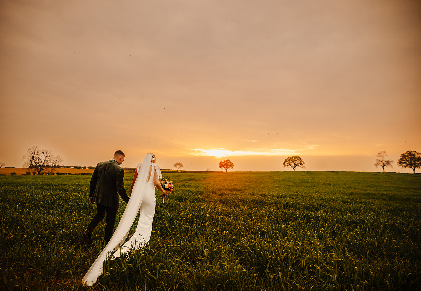 bride and groom walking through farm at golden hour