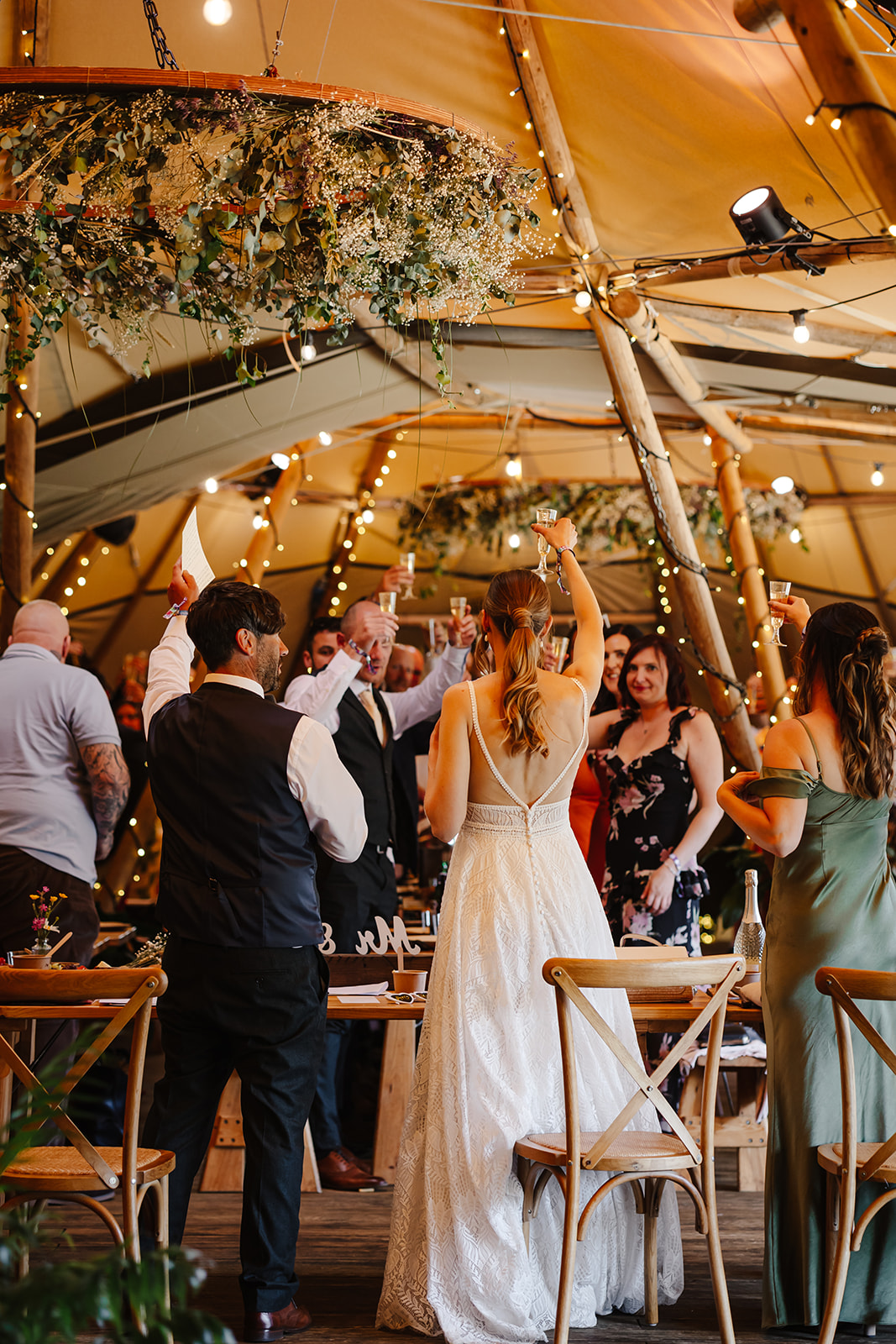 couple raising a toast in teepee wedding with fairy lights