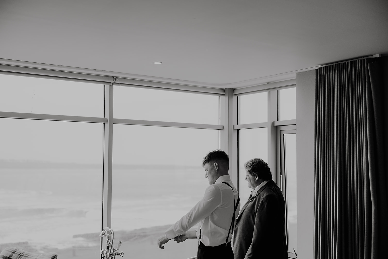 Ross getting ready beside a sea-facing window, photographed in black and white
