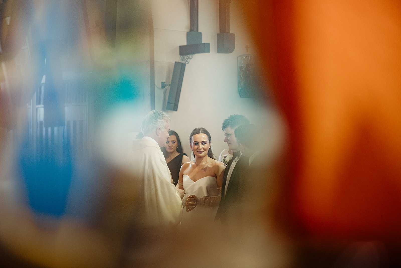 Alison and Ross exchanging vows, framed through colour in the church
