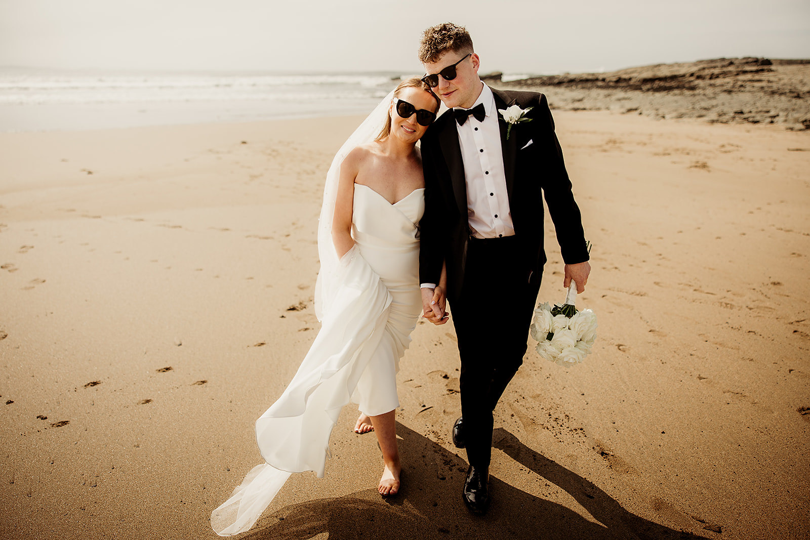 Alison and Ross walking along the beach together in sunglasses