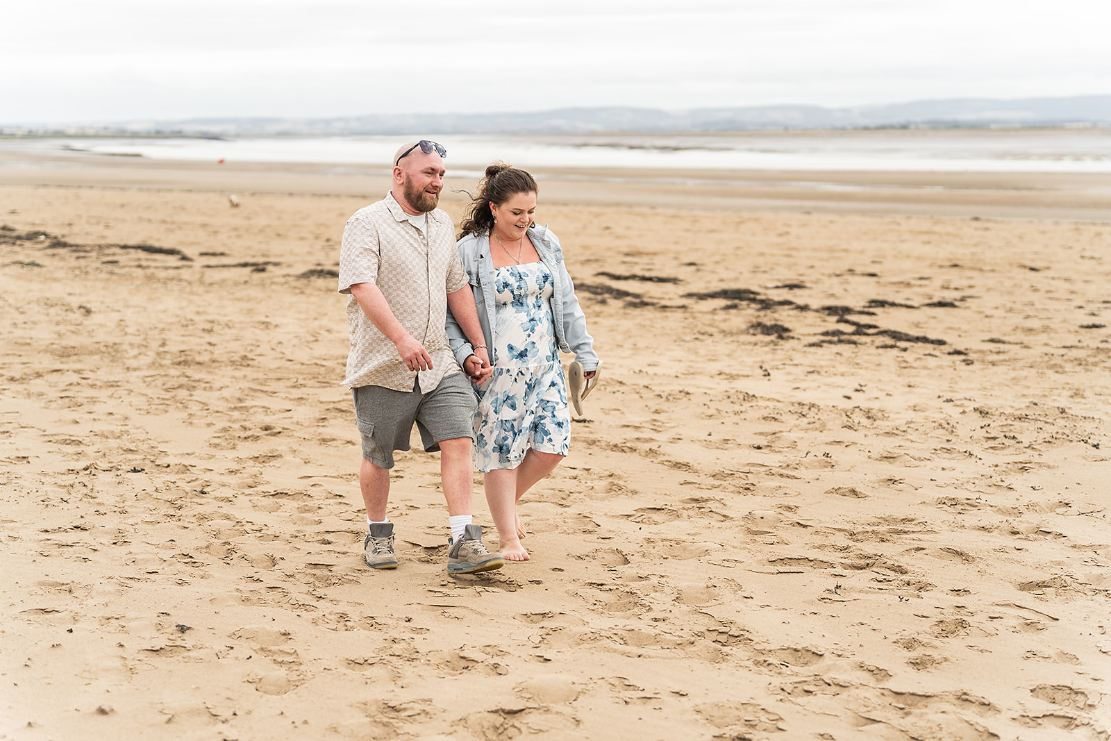 A couple strolling hand in hand across a wide sandy beach