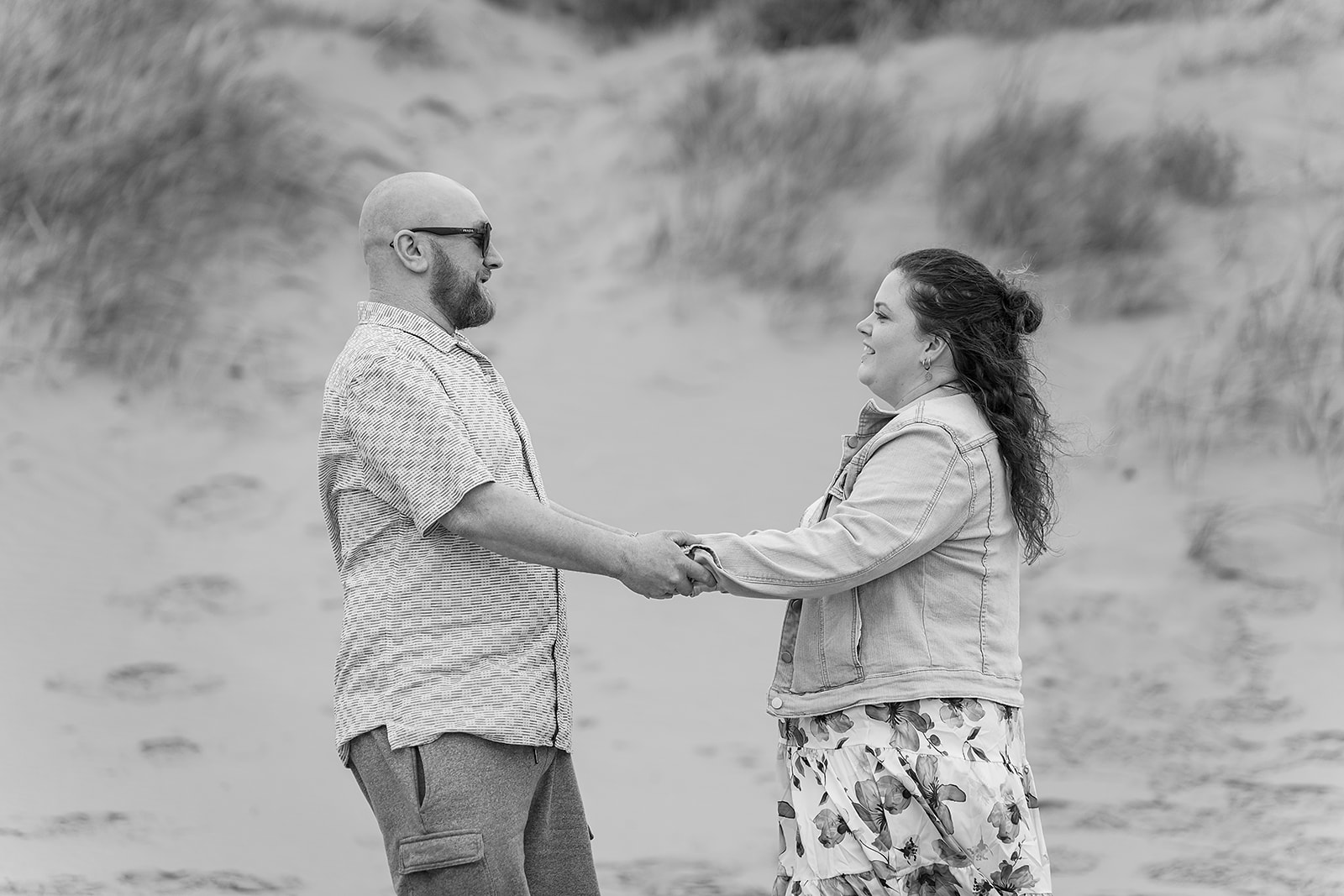 A couple holding hands among the sand dunes, in black and white