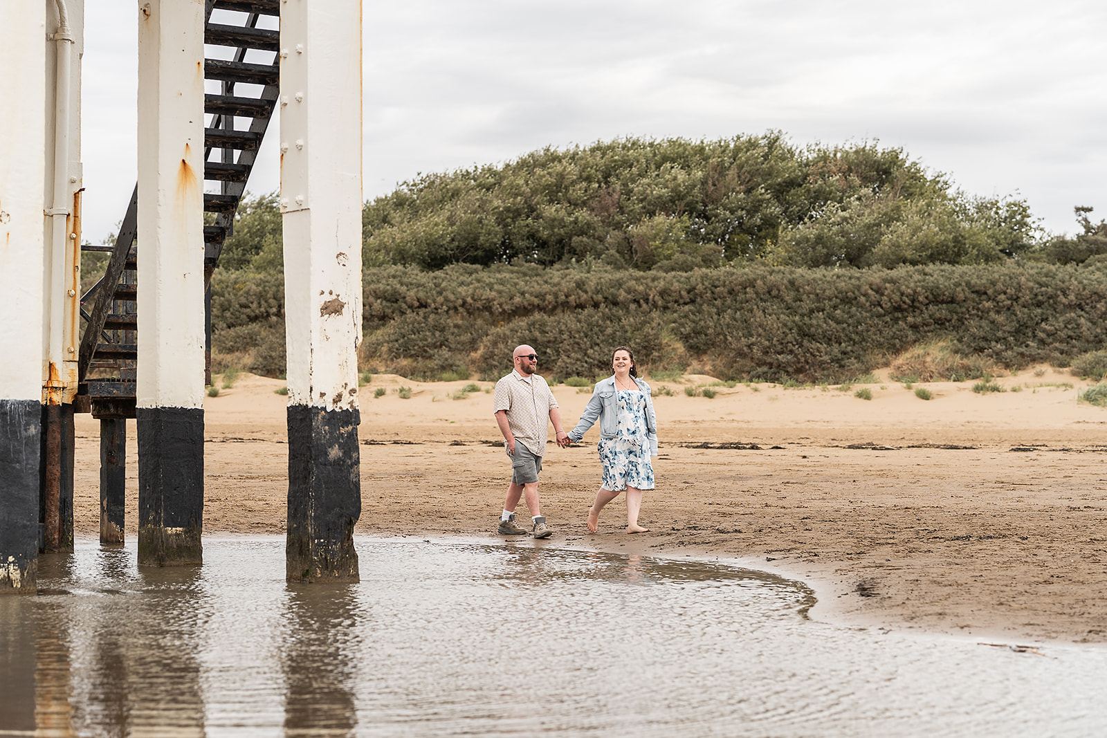 A couple on wet sand beside the reflections of a wooden lighthouse