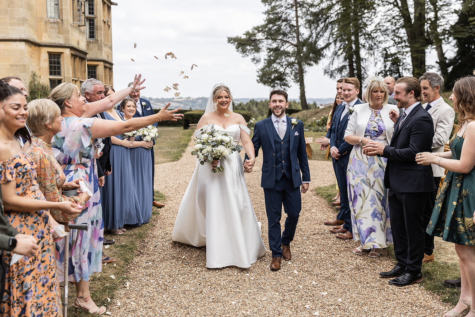 Newlyweds walking through a shower of flower-petal confetti as guests cheer