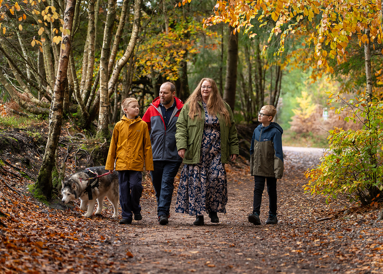 A family walking with their dog along an autumn woodland path