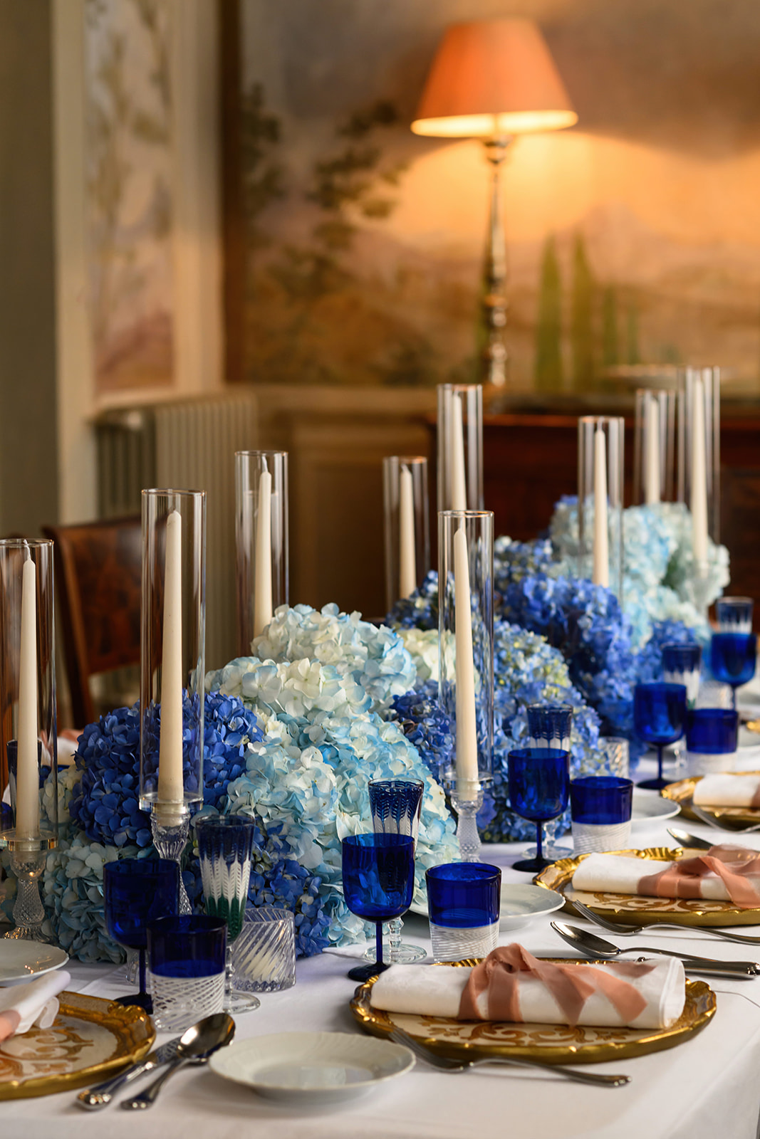 Wedding dinner table with blue hydrangeas, blue glassware and candles in a Tuscan villa