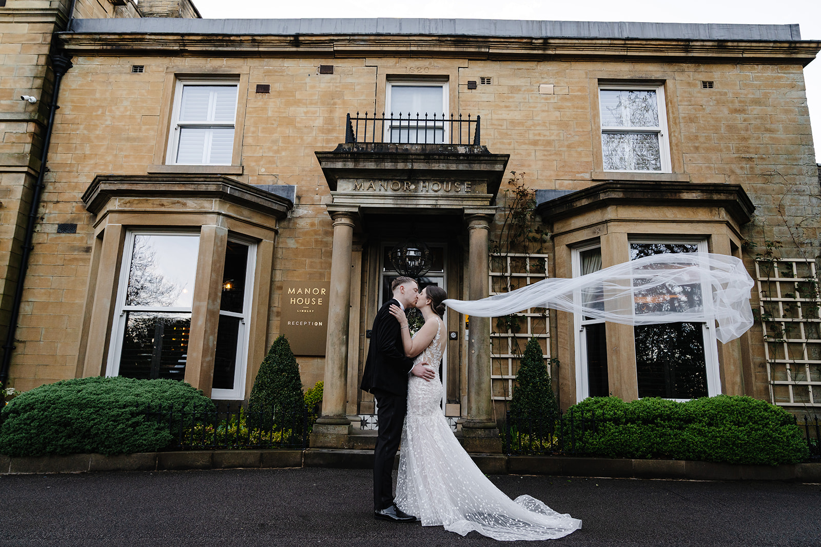 Abigail and Ben kissing outside Manor House Lindley with her veil in the air