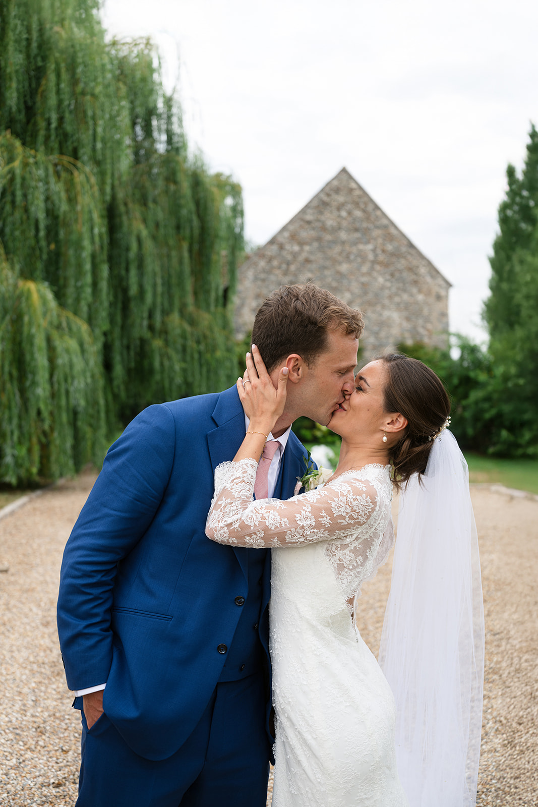 Bride and groom kissing in front of a stone barn at a French countryside wedding